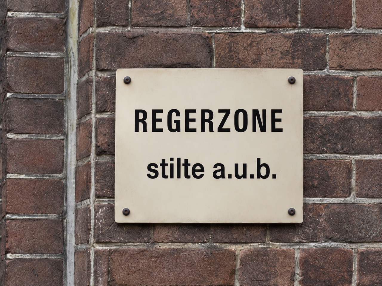Een bord met de tekst Regerzone, stilte a.u.b., aan een bakstenen muur.